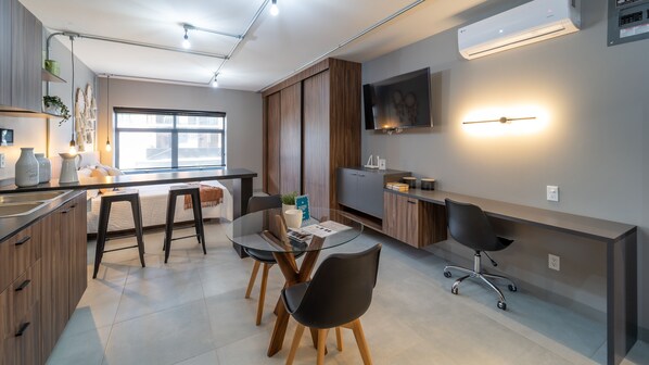 A modern kitchen with a dining area, featuring a large window, wooden cabinets, and a flat-screen TV. - Tribu San Martín Chapultepec (Guadalajara)