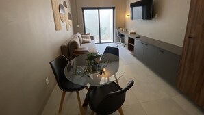 Un espacio habitable moderno con comedor, sofá, televisor y puerta corrediza de vidrio que da a un balcón.