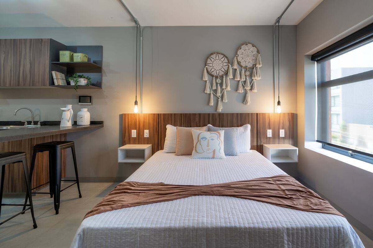 Un dormitorio moderno con una cama grande, mesitas de noche, un escritorio y una ventana.