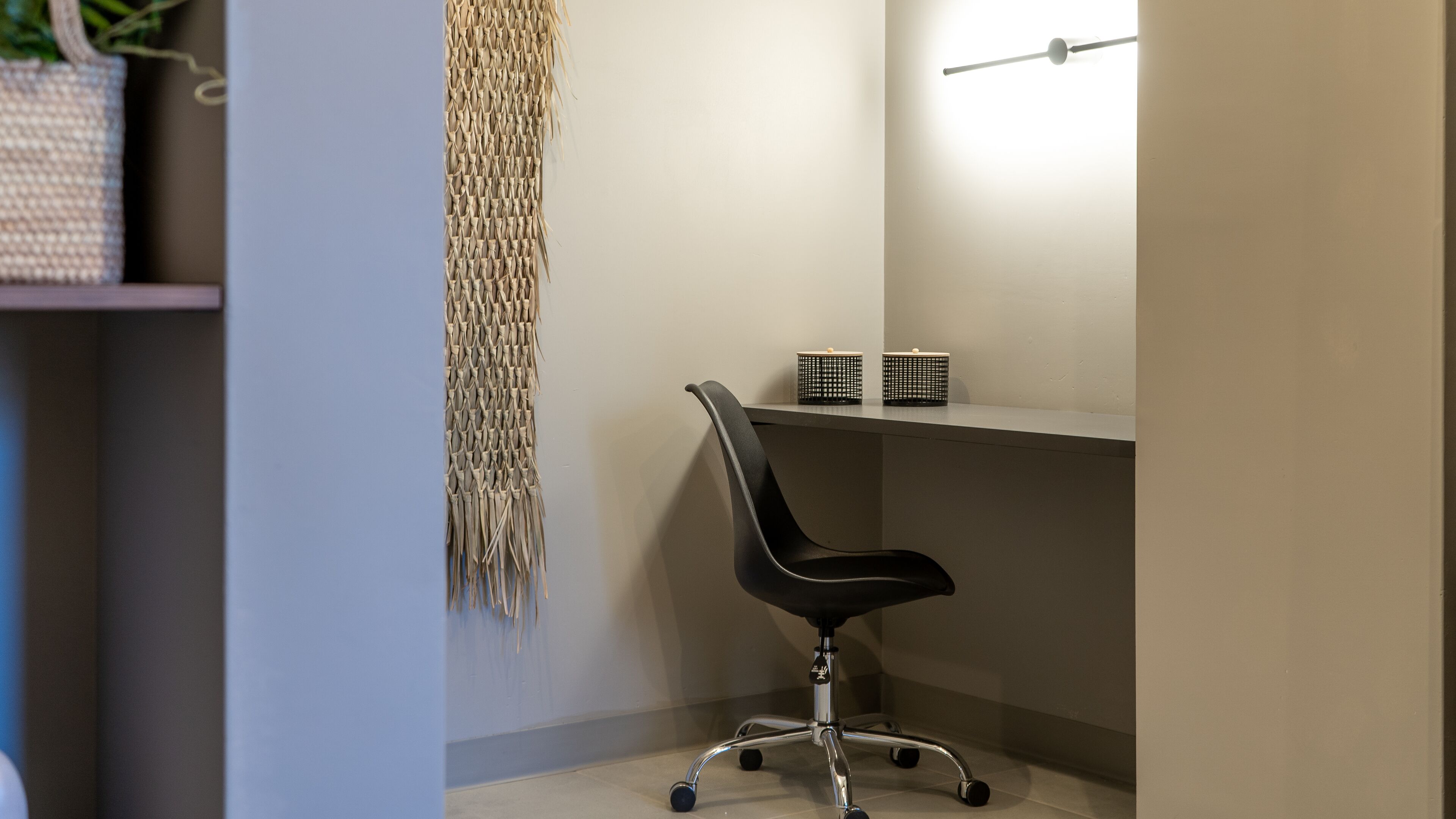A modern office chair with wheels, a woven wall hanging, and two black storage boxes on a shelf.