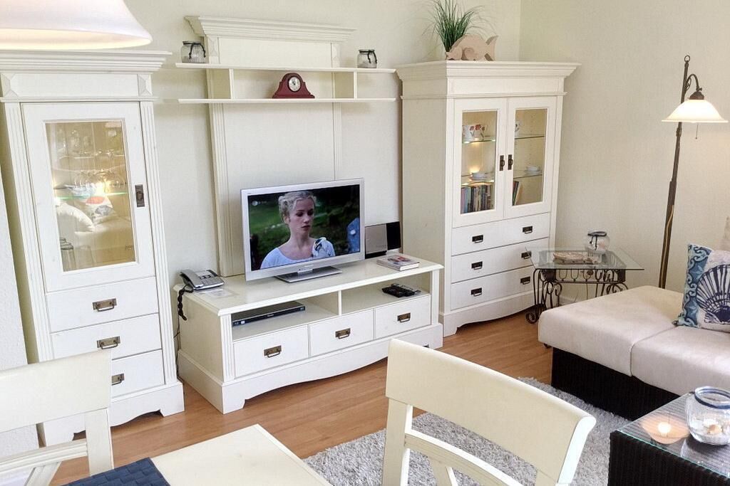 A living room with a television, white cabinets, a glass coffee table, and a sofa.