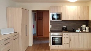 A compact kitchen with wooden cabinets, a built-in oven, a microwave, and a coffee maker.