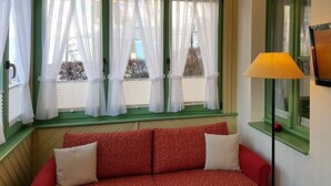 A room with a red sofa, white curtains, and a lamp.