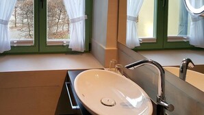 A bathroom with a large oval sink, a mirror, and a window with curtains.