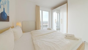 Habitación de hotel con una cama grande, una lámpara de noche, un cuadro en la pared y vistas al balcón.