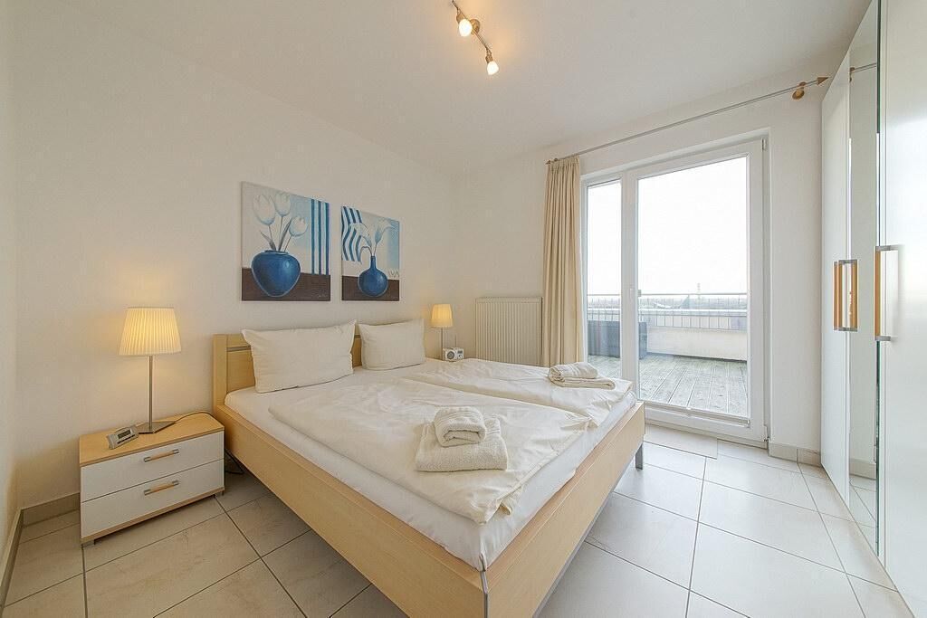 A hotel room with a large bed, two bedside tables, a window with a view, and artwork on the wall.