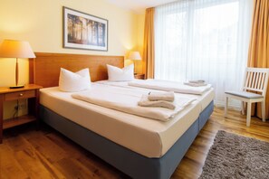A hotel room with a double bed, two bedside lamps, a chair, a window with curtains, and a painting on the wall. - 3-zimmer Ferienwohnung mit Sonnigem Balkon in Erstklassiger Lage am Ostseestrand (Heringsdorf)