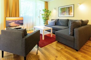 A living room with a grey sofa, a white coffee table, a grey armchair, a flat-screen TV, a red rug, a plant, and a framed picture on the wall. - 3-zimmer Ferienwohnung mit Sonnigem Balkon in Erstklassiger Lage am Ostseestrand (Heringsdorf)