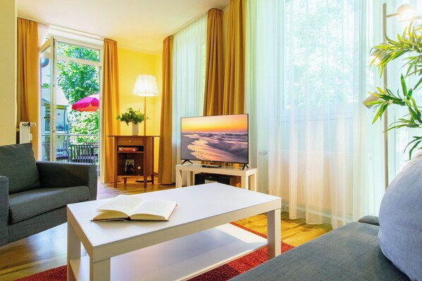 A modern living room with a sofa, a coffee table, a TV, and a view of the outdoors. - 3-zimmer Ferienwohnung mit Sonnigem Balkon in Erstklassiger Lage am Ostseestrand (Heringsdorf)
