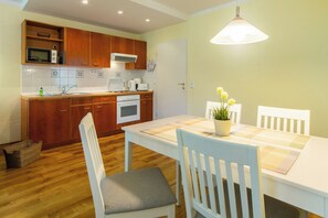 A kitchen with wooden cabinets, a white countertop, a sink, a microwave, a stove, and a dining table with chairs. - 3-zimmer Ferienwohnung mit Sonnigem Balkon in Erstklassiger Lage am Ostseestrand (Heringsdorf)