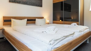 A modern hotel room with a wooden bed frame, white bedding, and a large mirror reflecting the room. - Apartment mit Sauna, Whirlbadewanne und Balkon an der Graft mit Blick zum Deich! (Nordseeheilbad Schillig)