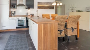 A modern kitchen with a central island, built-in oven, and a dining area with wicker chairs. - Apartment mit Sauna, Whirlbadewanne und Balkon an der Graft mit Blick zum Deich! (Nordseeheilbad Schillig)
