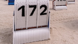 A beachside hotel with numbered beach chairs, a lifeguard stand, and a clear view of the ocean. - Apartment mit Sauna, Whirlbadewanne und Balkon an der Graft mit Blick zum Deich! (Nordseeheilbad Schillig)