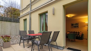 A patio with a table and chairs, a door leading to an interior room, and a small garden area with plants.