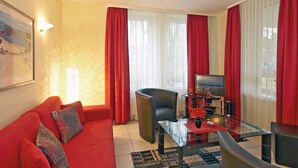 A modern living room with a red sofa, a glass coffee table, and a black armchair.