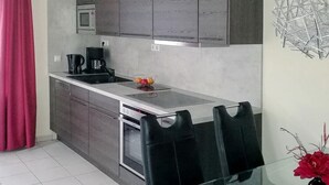 A compact kitchen with grey cabinets, a microwave, a coffee maker, and a bowl of fruit on the counter.