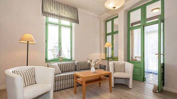 A living room with a sofa, two armchairs, a wooden coffee table, and two lamps. - 4-zimmer Ferienwohnung mit Wintergarten und Terrasse in Toplage an der Promenade (Heringsdorf)