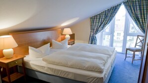 Een hotelkamer met een groot bed, twee nachtkastjes met lampen, een stoel en uitzicht op gebouwen door het raam.