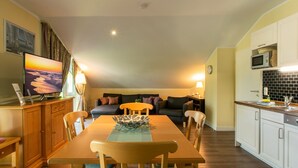 Een eethoek met een houten tafel en stoelen, een televisie op een kast, en een keuken met witte kasten en een magnetron.