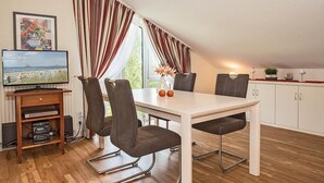 A dining area with a white table, four chairs, a television on a wooden shelf, and a window with curtains. - Cozy, charming top floor vacation apartment in an excellent beach location (Heringsdorf)