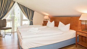 A hotel room with a large bed, two bedside tables, a chair, and a window with curtains. - Cozy, charming top floor vacation apartment in an excellent beach location (Heringsdorf)