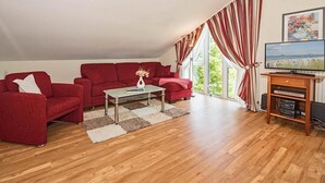 A living room with a red sofa set, a coffee table, and a TV on a wooden stand. - Cozy, charming top floor vacation apartment in an excellent beach location (Heringsdorf)