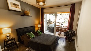 A bedroom with a bed, bedside lamps, a small table, a chair, and a view of an outdoor patio. - New accommodation, summer kitchen, terrace, garden (Olmeto)