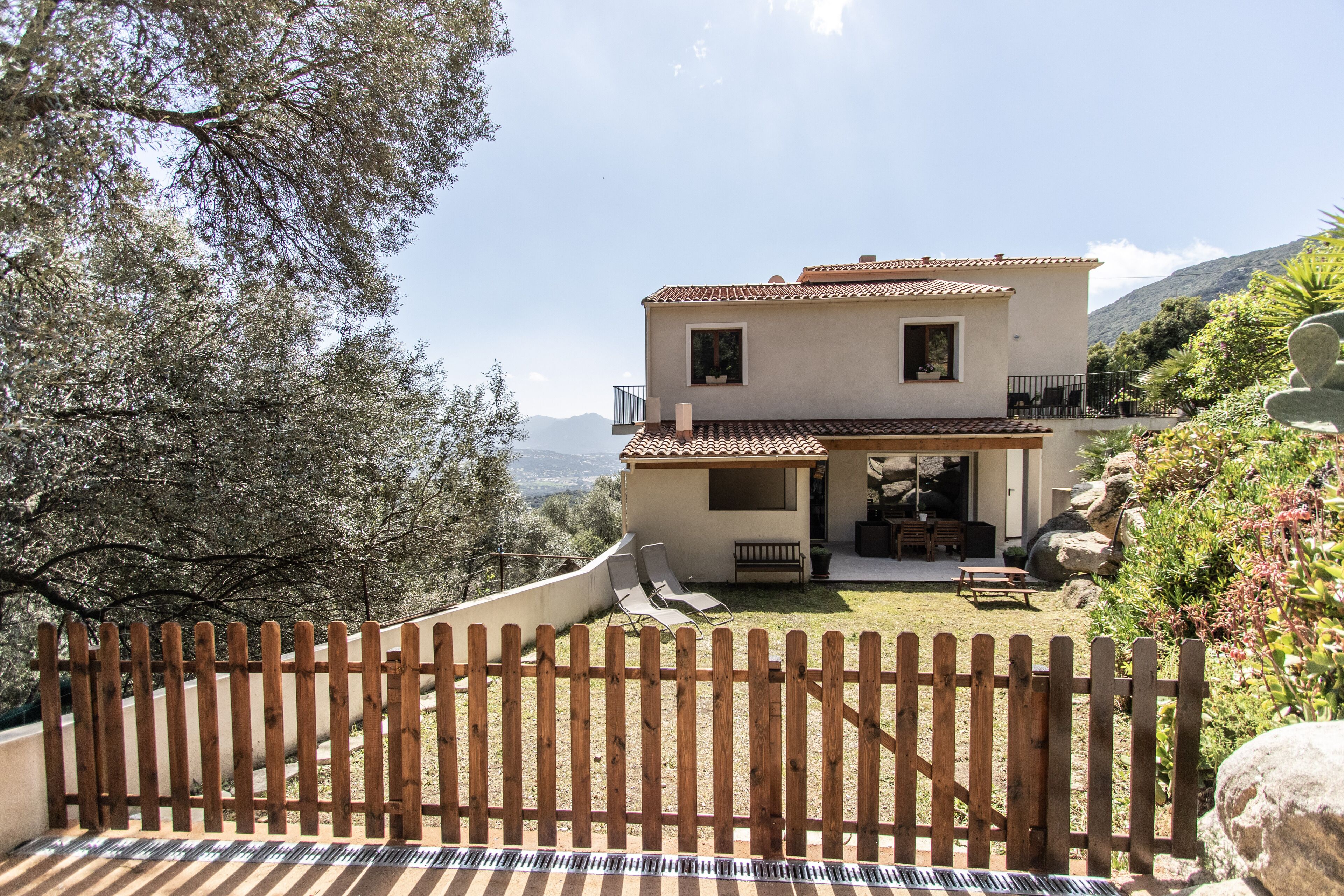 A two-story house with a patio, a wooden fence, and a view of the mountains.