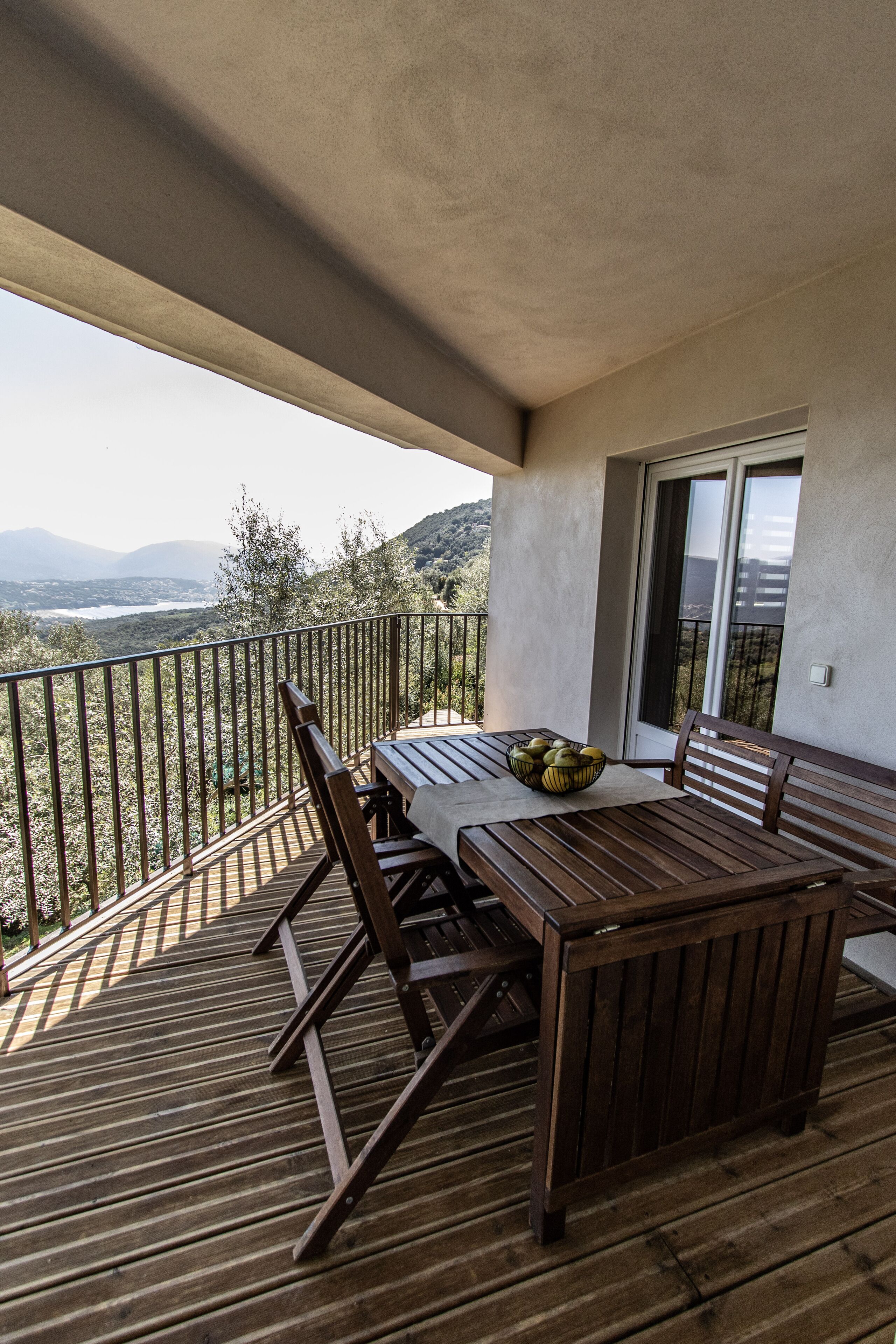 A wooden deck with a table and chairs, a bowl of fruit, and a view of the mountains.
