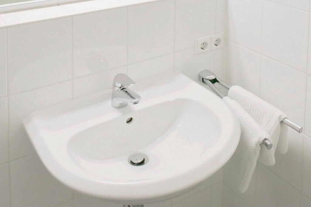 Un lavabo blanco con grifo cromado, un perchero y una toalla blanca colgada.