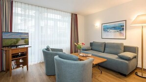 Una sala de estar moderna con un sofá, dos sillones, una mesita de centro, un televisor y un cuadro en la pared.