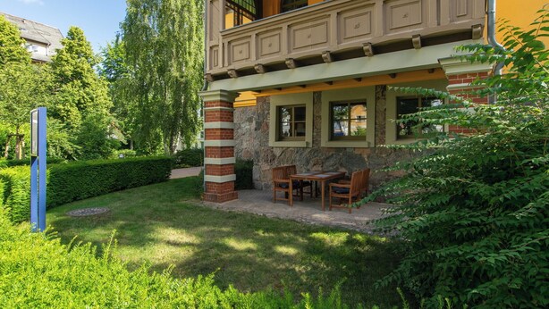 A two-story building with a balcony, stone columns, and a patio area with outdoor furniture.