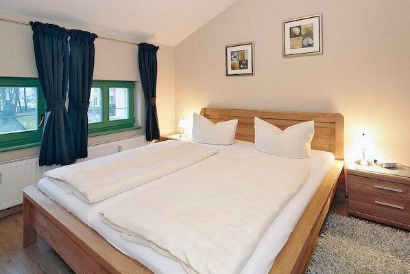 A neatly made bed with white linens, a wooden headboard, and two bedside tables with lamps.