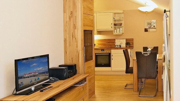 A compact living space with a wooden entertainment unit, a kitchenette, and a dining area.