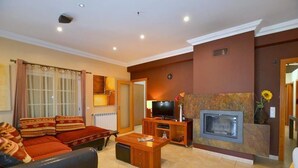 A living room with a sofa, coffee table, TV, fireplace, and a door leading to another room. - Kine Villa, Armação de Pêra, Algarve (Armação de Pêra)