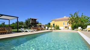 A swimming pool with lounge chairs, a wooden deck, and a yellow building with a tiled roof. - Kine Villa, Armação de Pêra, Algarve (Armação de Pêra)