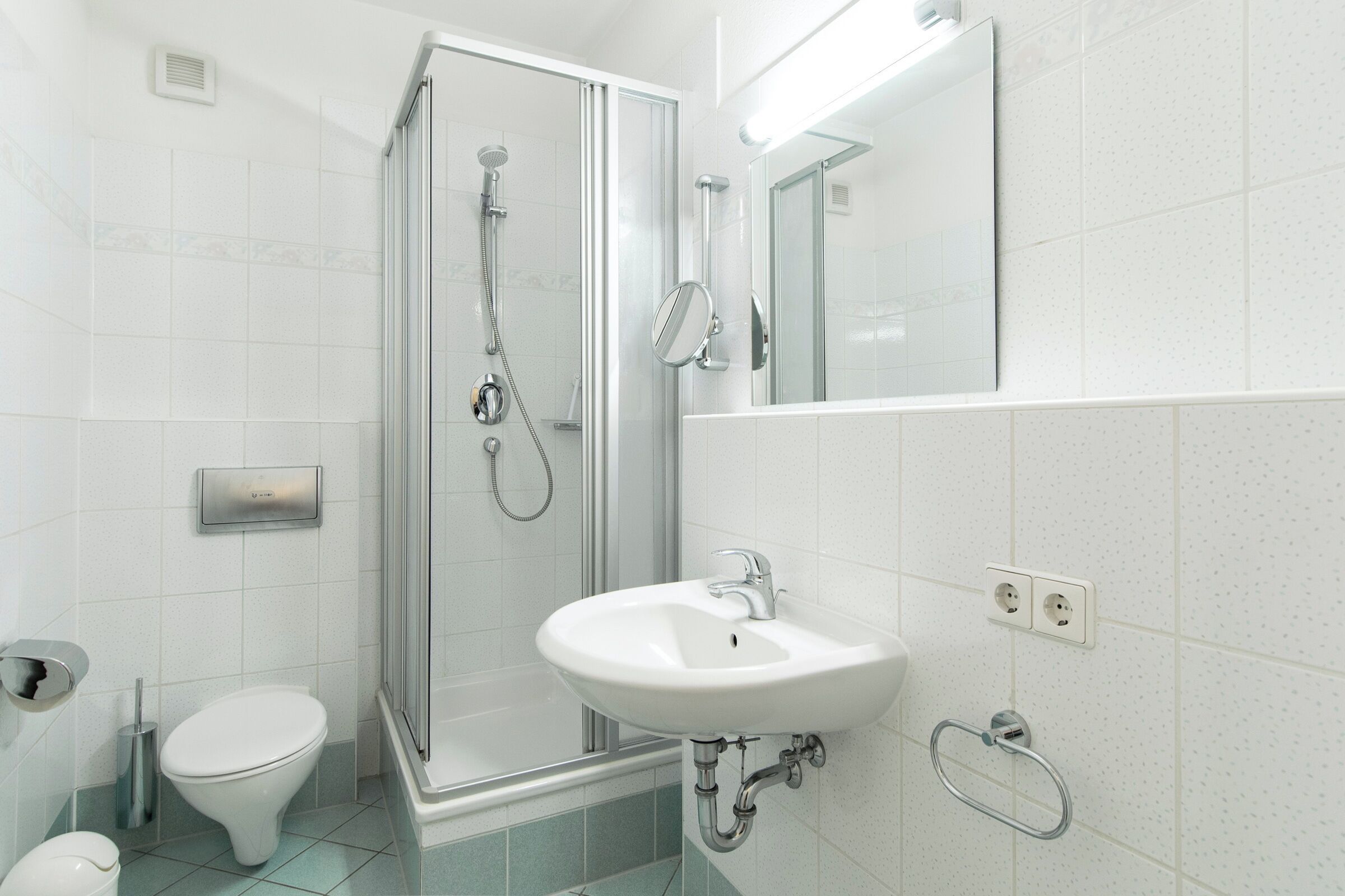 Een moderne badkamer met een douchecabine van glas, een witte wastafel en een toilet.