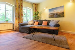 A living room with a sofa, a coffee table, a window with curtains, a radiator, and a painting on the wall.