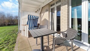 A patio with a table and chairs, a wicker chair, and a striped chair. - Hübsche, Strandnahe Ferienwohnung mit Eigener Sauna und Terrasse mit Strandkorb (Nordseebad Wremen)