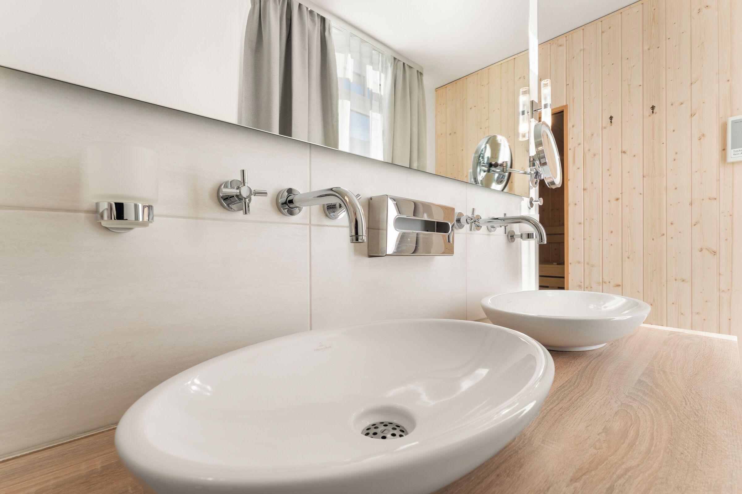 A modern bathroom with two white ceramic sinks, chrome fixtures, and a wooden panel wall.