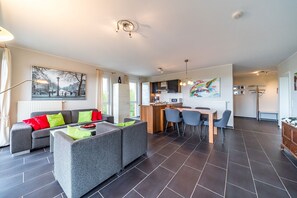 Un salon moderne avec un canapé, un coin repas avec des chaises et une cuisine en arrière-plan.