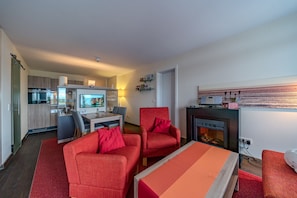 Una sala moderna con sofá, sillones y una mesa de centro. Se ve una cocina al fondo con un comedor.