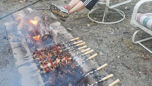 A person sitting by a grill with skewers of meat and vegetables. - Serenity between the lakes and seashore (Westbrook)
