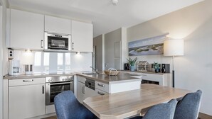 A modern kitchen with white cabinetry, a central island, and a dining area with two chairs.