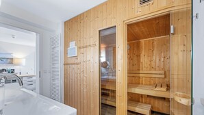 A modern bathroom with a wooden sauna, a large sink, and a glass-enclosed shower area.