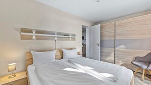 A modern bedroom with a bed, bedside table, lamp, and a chair.