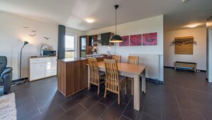 A modern kitchen with a dining area, featuring a wooden table and chairs, a microwave, and a view of the outdoors. - Exklusives Ferienapartment mit Meerblick, Balkon, Sauna und Whirlbadewanne (Nordseeheilbad Schillig)