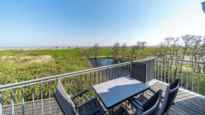 A balcony with a table and chairs overlooking a river and fields. - Exklusives Ferienapartment mit Meerblick, Balkon, Sauna und Whirlbadewanne (Nordseeheilbad Schillig)