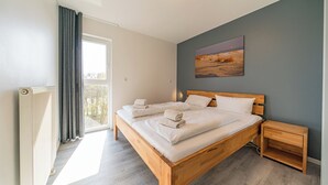 A bedroom with a large bed, a nightstand, a radiator, and a window with curtains. - Exklusives Ferienapartment mit Meerblick, Balkon, Sauna und Whirlbadewanne (Nordseeheilbad Schillig)