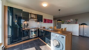 A modern kitchen with black cabinets, a built-in oven, a washing machine, and a wooden countertop. - Exklusives Ferienapartment mit Meerblick, Balkon, Sauna und Whirlbadewanne (Nordseeheilbad Schillig)